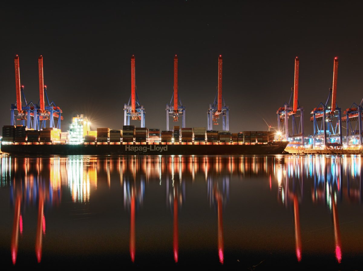 Container terminal cranes lit at night, reflected in the harbour